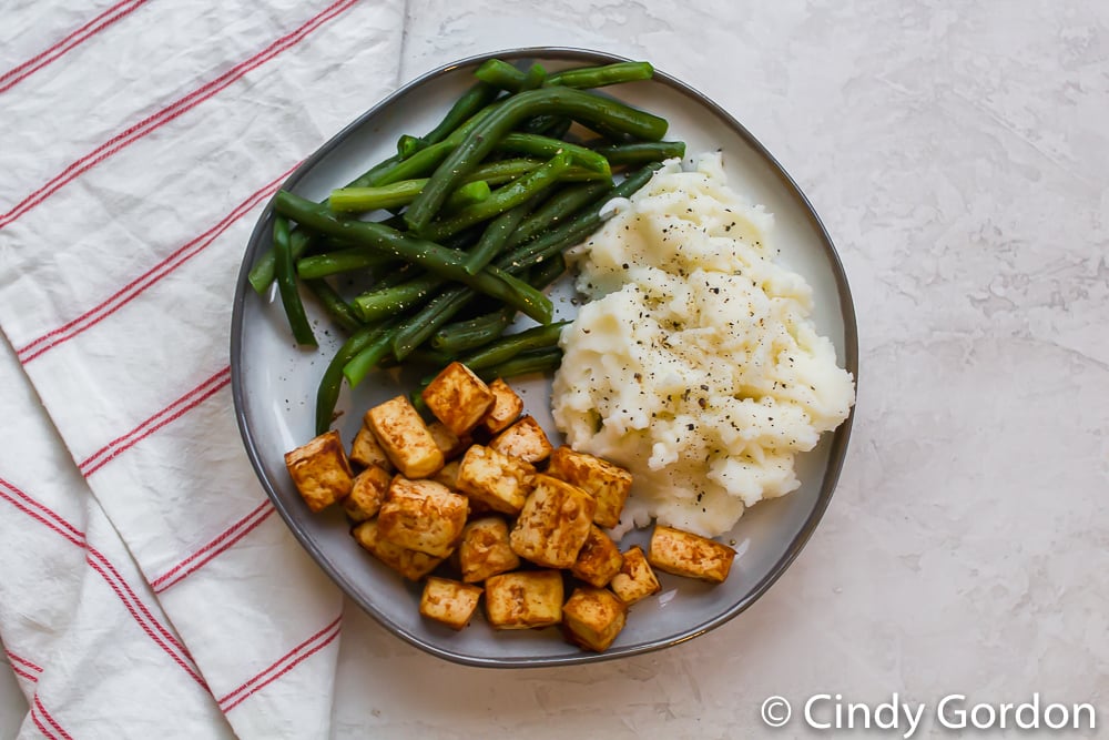 tofu squares with mashed potatoes and green beans on a round gray plate