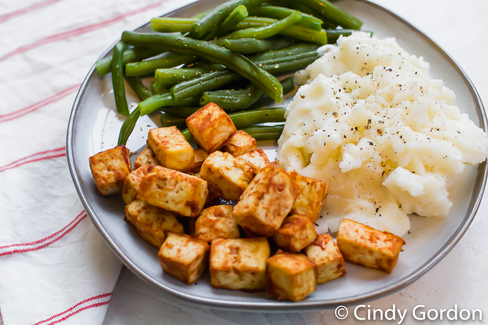 barbecue tofu squares on a plate with mashed potatoes and green beans