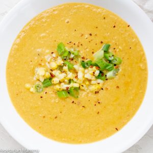 Yellow soup in a white bowl and a white towel with red stripes to the right