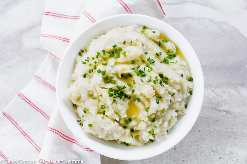 a white bowl filled with mashed potatoes garnished with melted butter and chives