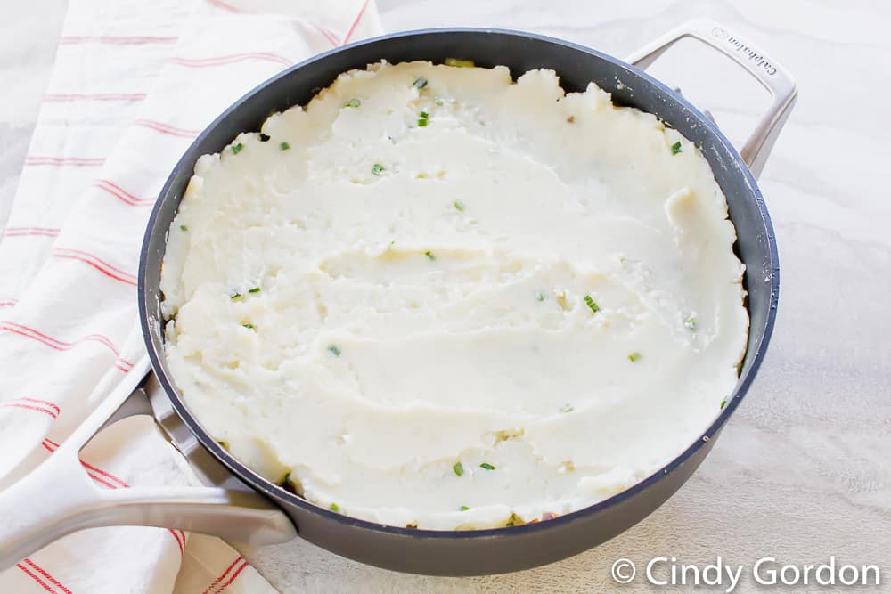 a skillet with mashed potatoes studded with chives smoothed across the pan
