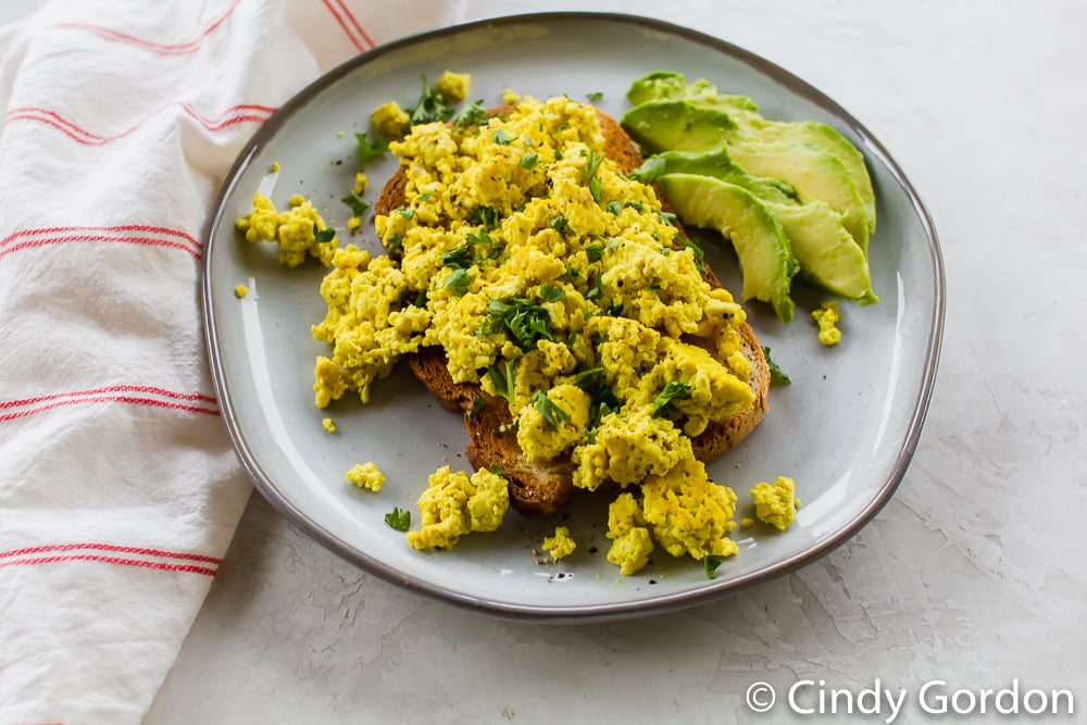 tofu scramble over toast with avocado slices on a white plate