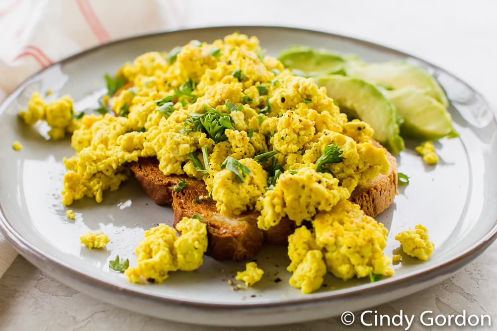 tofu scramble over toast with avocado slices on a white plate