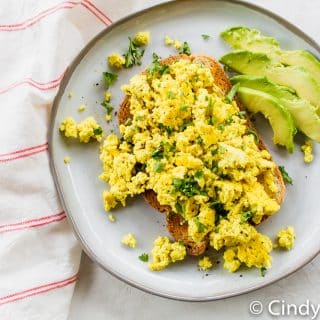 tofu scramble over toast with avocado slices on a white plate