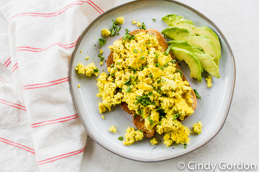 tofu scramble over toast with avocado slices on a white plate