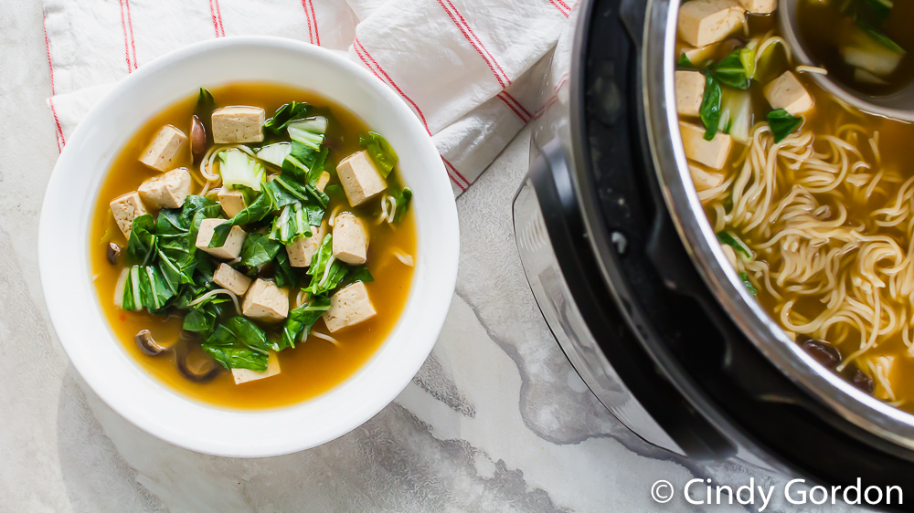 a bowl of ramen soup on a marble countertop next to an open Instant Pot