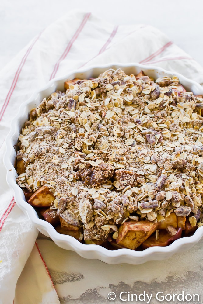 a pie pan of vegan apple crisp with a red striped kitchen towel
