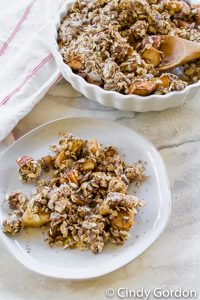 apple crisp in a pie pan next to a white plate being served