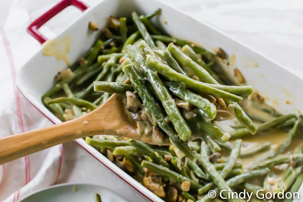 green bean casserole being served from a baking dish with a wooden spoon