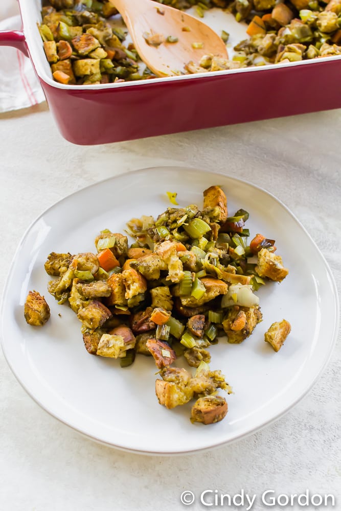 stuffing on a white plate next to a red baking dish