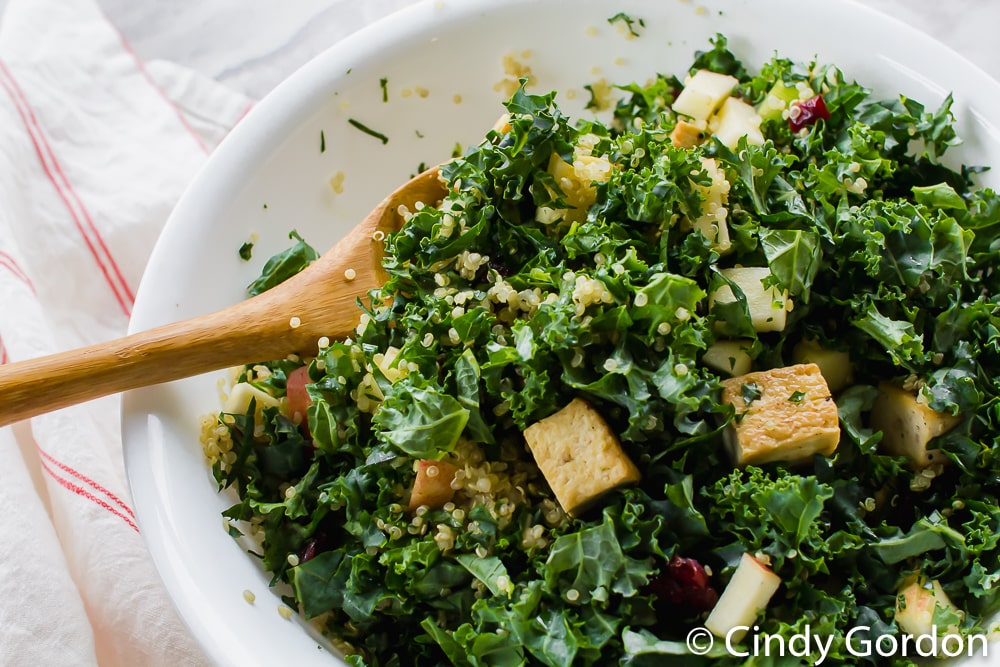 Overhead shot of a kale and tofu salad in a white bowl with a wooden spoon