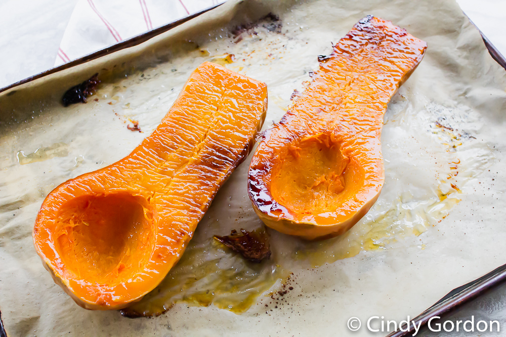 A roasted butternut squash on a piece of parchment paper over a baking sheet