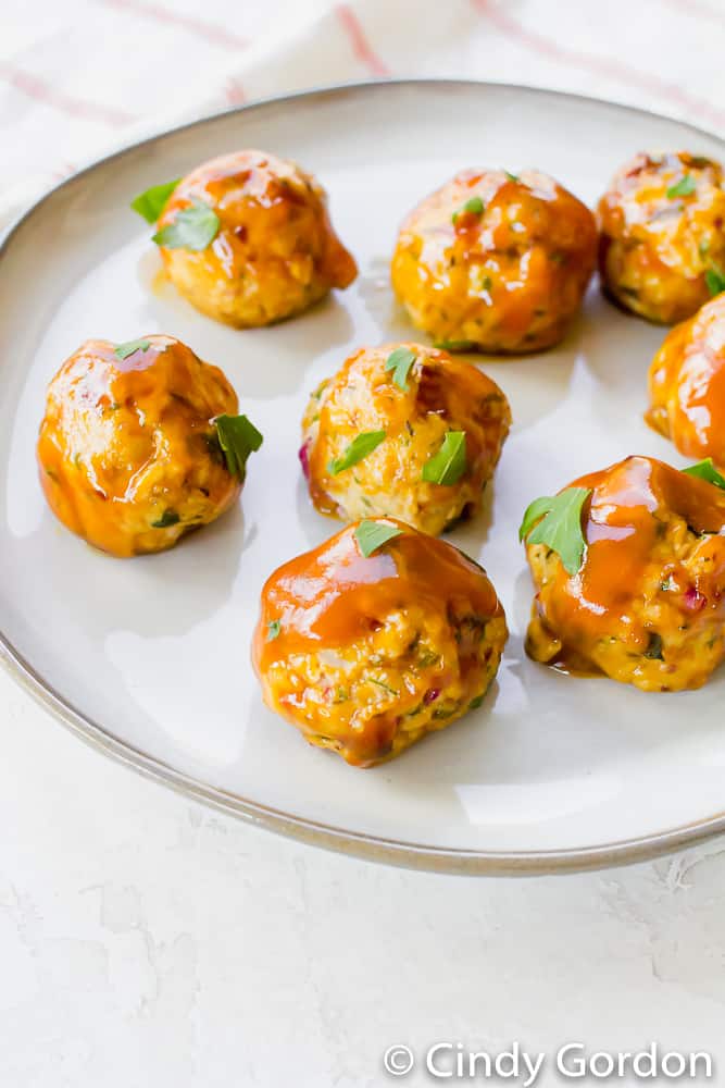 Eight vegan meatballs on a white plate drizzled with sauce and garnished with parsley