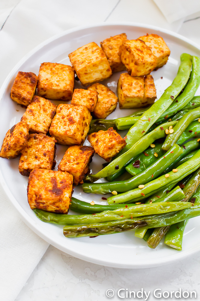 Baked tofu and seasoned green beans on a white plate on a marble countertop