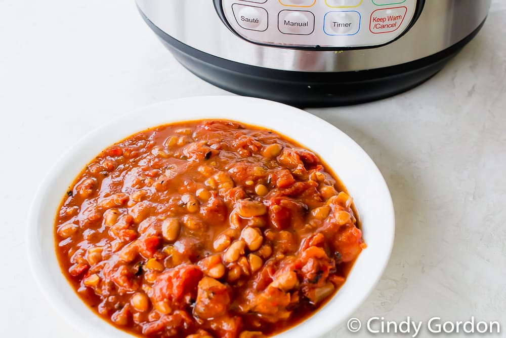 A white round bowl of vegetarian chili next to a pressure cooker