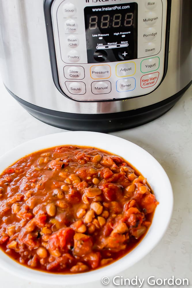 A white bowl of vegan chili next to an Instant Pot pressure cooker