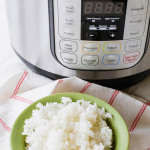 A green bowl of white rice in front of a pressure cooker