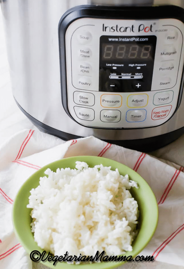 A green bowl of white rice in front of a pressure cooker