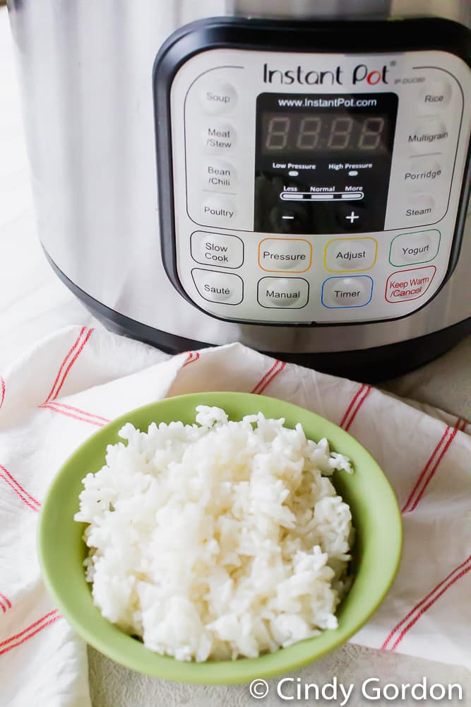 A green bowl of white rice in front of a pressure cooker