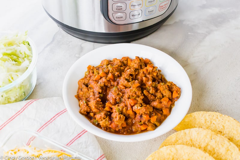 Vegetarian taco meat in a bowl next to an Instant Pot, lettuce, and taco shells