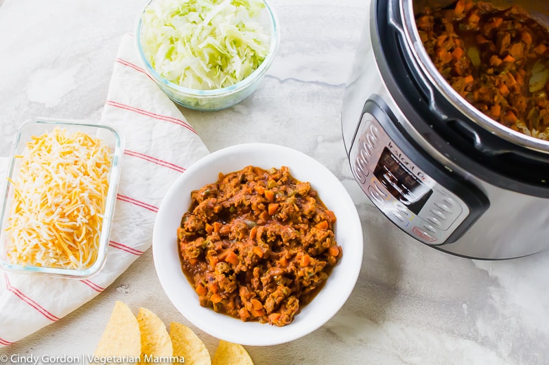 Taco meat in an Instant Pot and in a white bowl with taco toppings