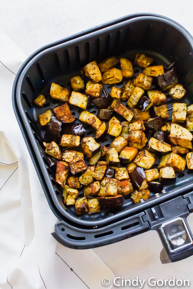 cubed eggplant in black air fryer basket. air fryer basket is tilted a little to the left.