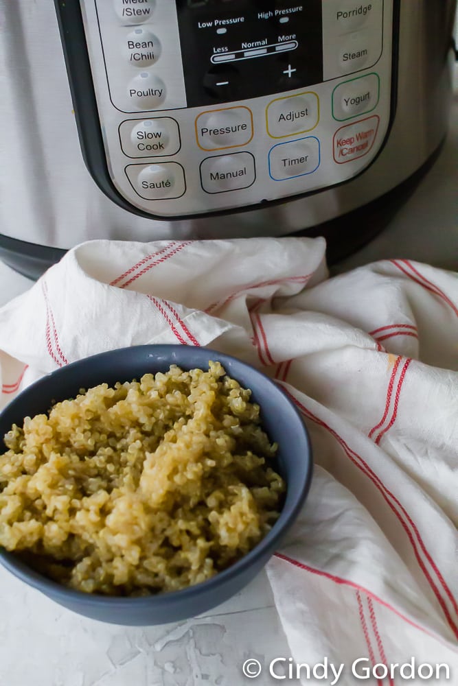 A blue bowl of cooked quinoa in front of an Instant Pot