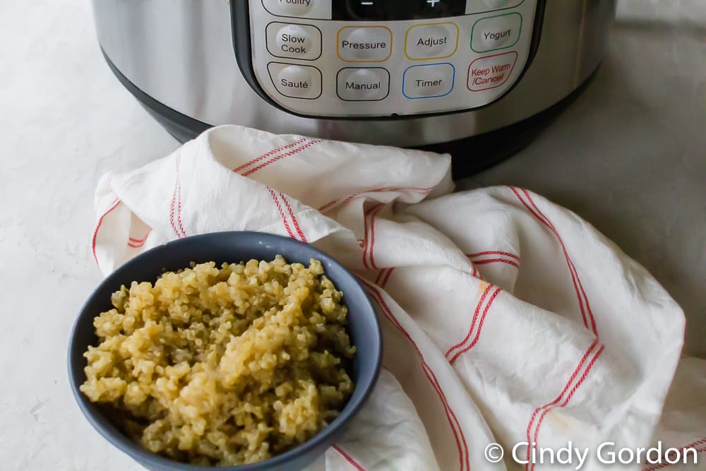 Quinoa in a bowl with an Instant Pot and a white and red striped kitchen towel