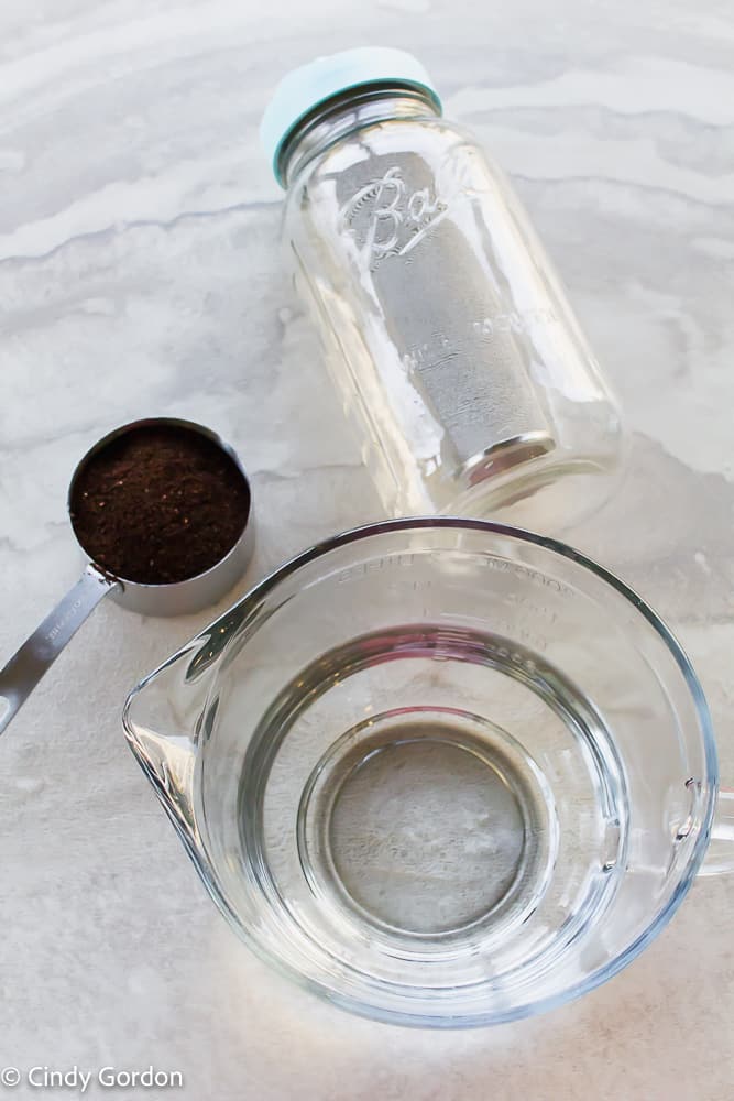 mason jar cold brew ingredients. Coffee grounds in a measurement cup, a big glass measuring cup of water and a mason jar with a teal lid