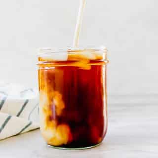 vertical photo of brown coffee in a mason jar and white liquid being poured into the jar