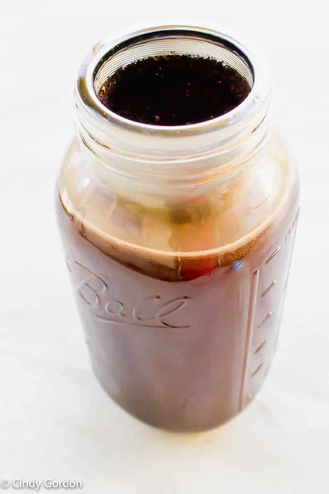 2 quart glass mason jar with metal mesh filter inside filled with coffee ground. Liquid in jar is brown. looks like coffee