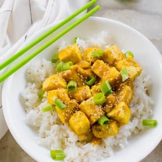 Vegan orange chicken in a white bowl with green chopsticks