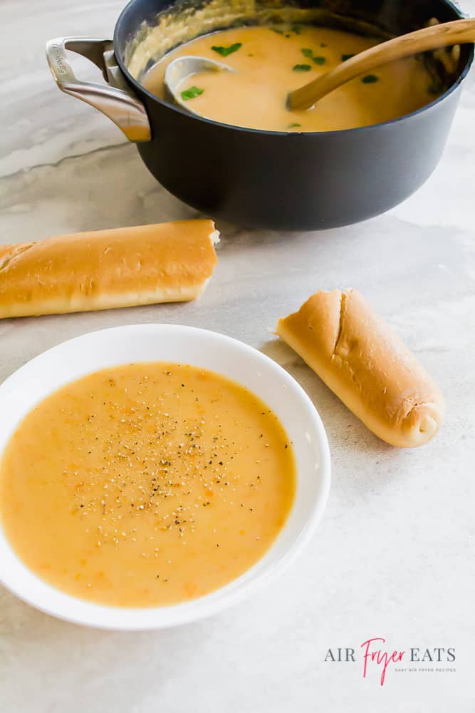 A bowl of vegan potato soup garnished with black pepper with a pot and bread