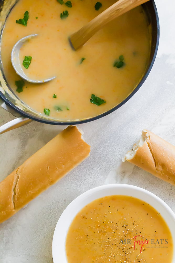 A pot and a bowl of vegan potato soup with a ripped baguette