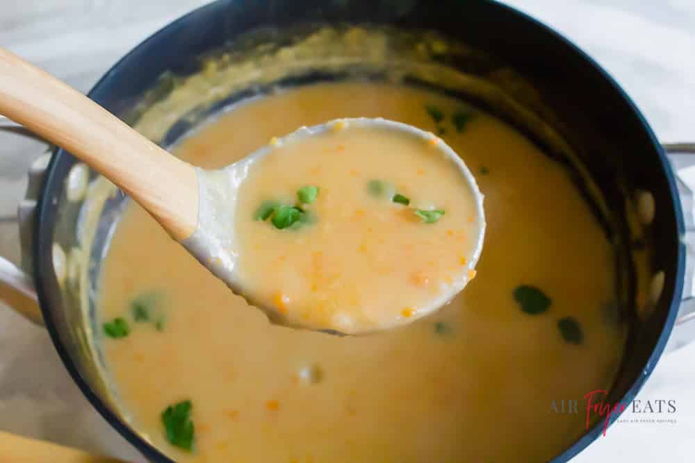A ladle full of vegan potato soup over the pot garnished with parsley