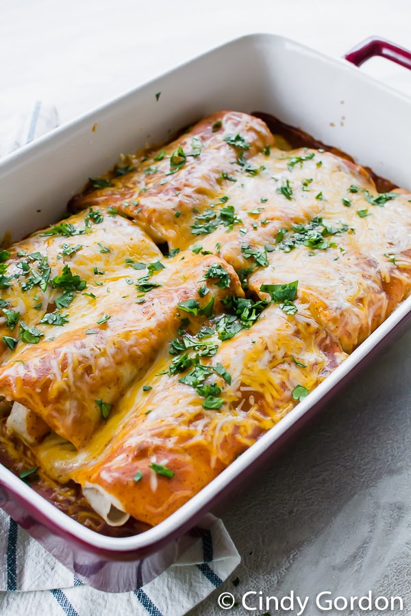 A red and white baking dish with enchiladas topped with cheese and cilantro