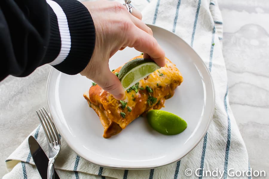 Someone squeezing lime juice onto a vegetarian enchilada on a white plate