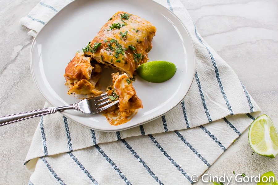 A bite of enchilada on a fork on a white plate with a lime wedge