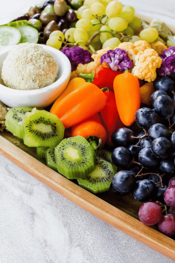 wooden brown platter loaded with colorful fruits, vegetables and crackers