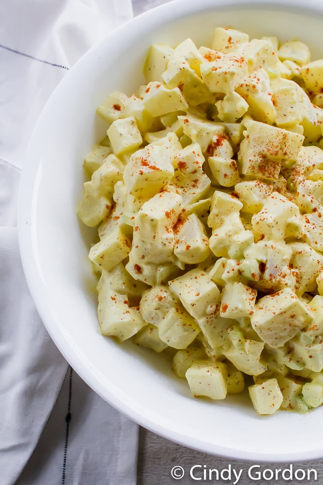 Close-up top shot of creamy potato salad in a white bowl with paprika