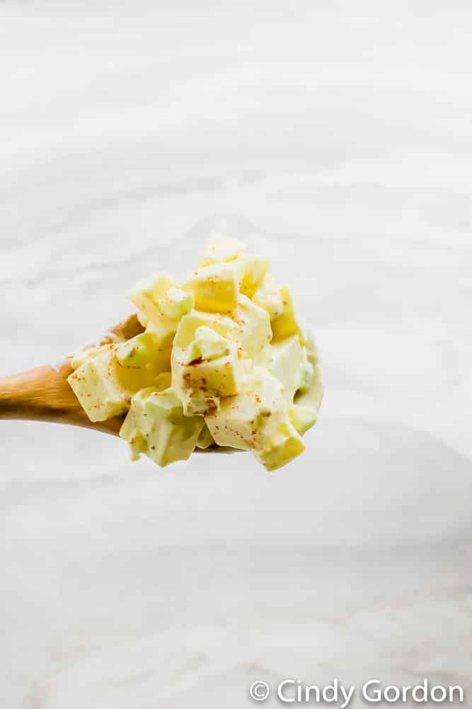 A wooden spoonful of potato salad over a marble countertop