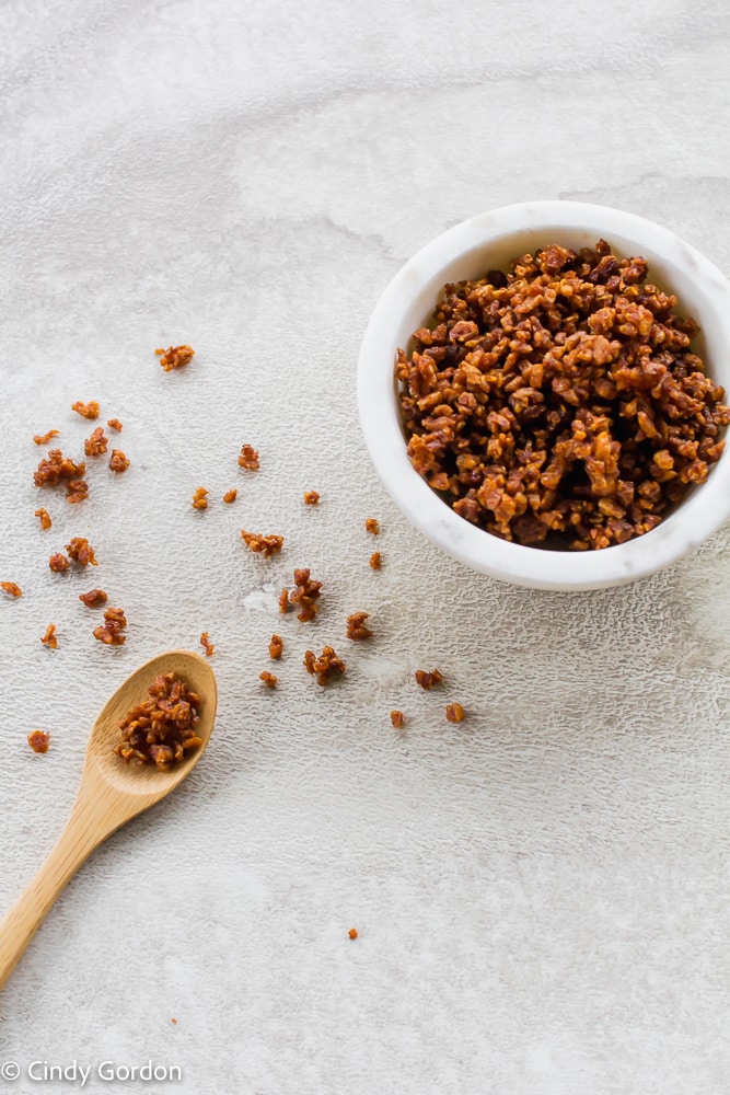 Vegan bacon bits scattered on the counter with a wooden spoon and a white bowl