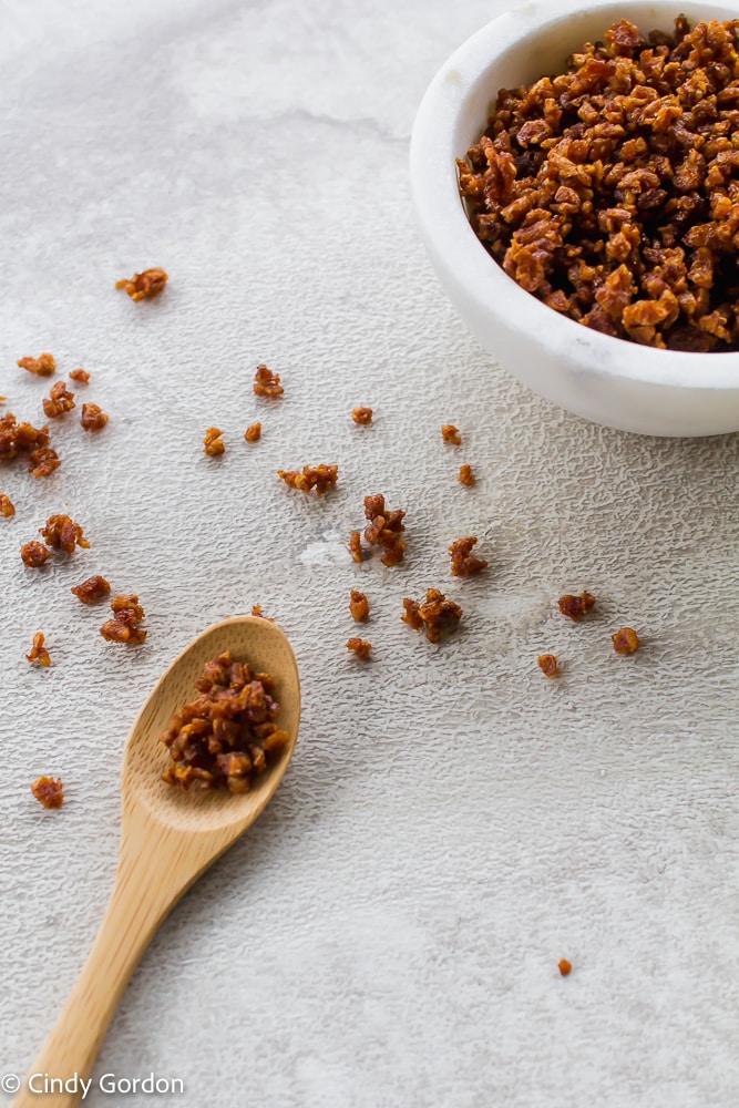 Vegan bacon bits in a white bowl and in a wooden spoon on a countertop