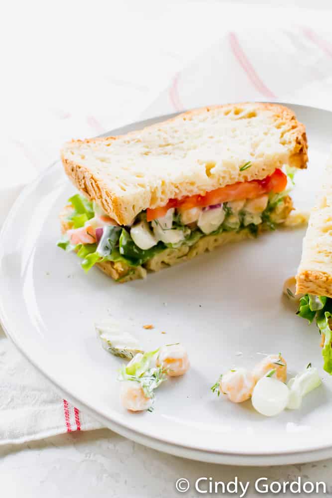 Vegan chickpea salad on vegan bread with tomato and lettuce on a white plate