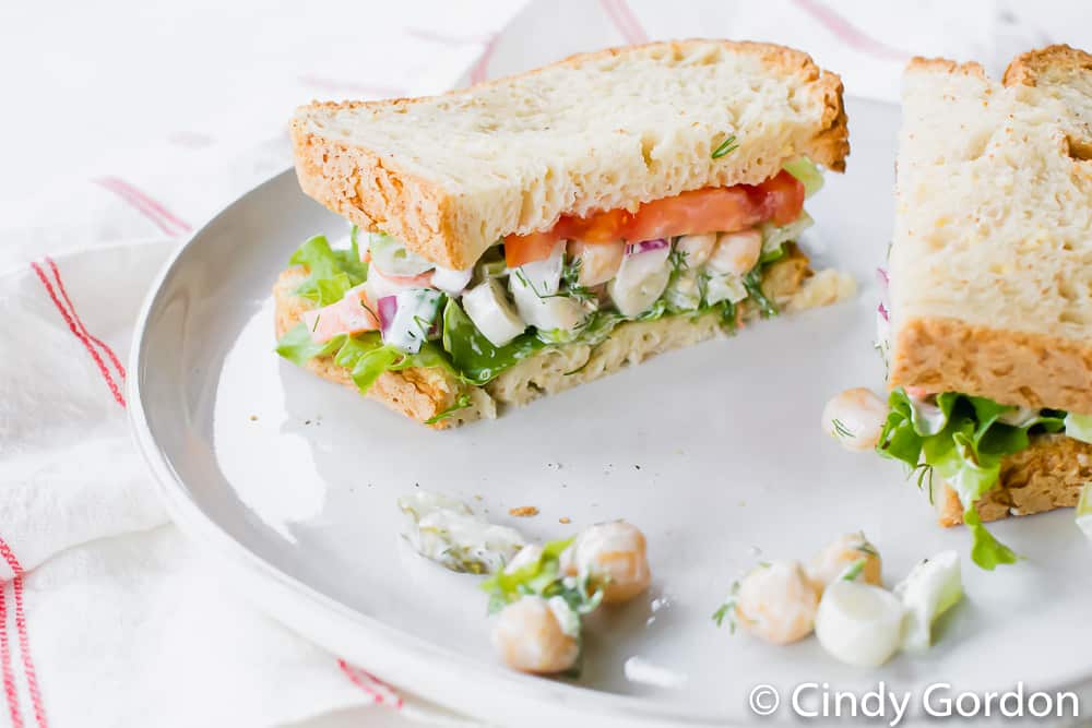 A vegan chickpea salad sandwich with lettuce and tomato on a white plate