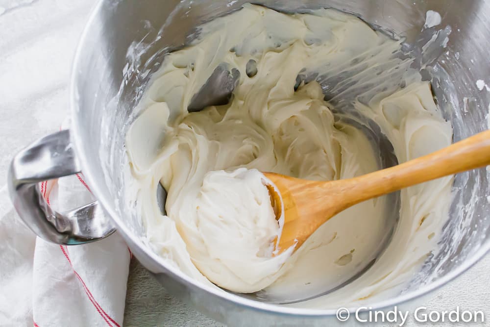 A mixing bowl of white frosting with a wooden spoon