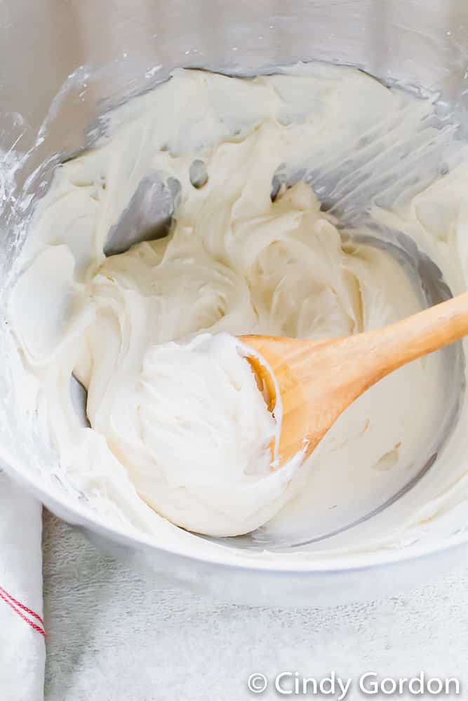 White frosting in a mixing bowl with a wooden spoon