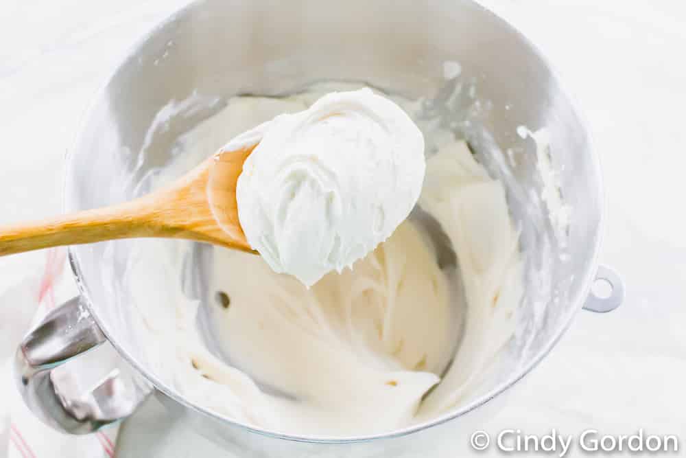 A wooden spoon of vegan frosting over a mixing bowl with more frosting