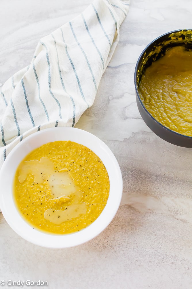 A white bowl of grits with vegan butter next to a sauce pot