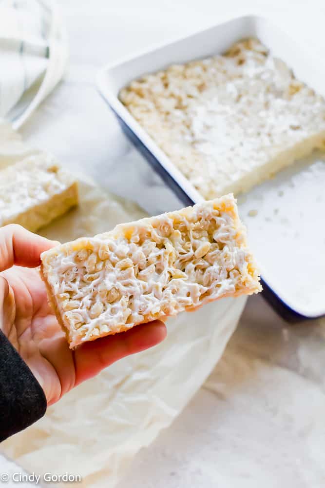 A vegan rice crispy treat in someone's hand above a baking dish